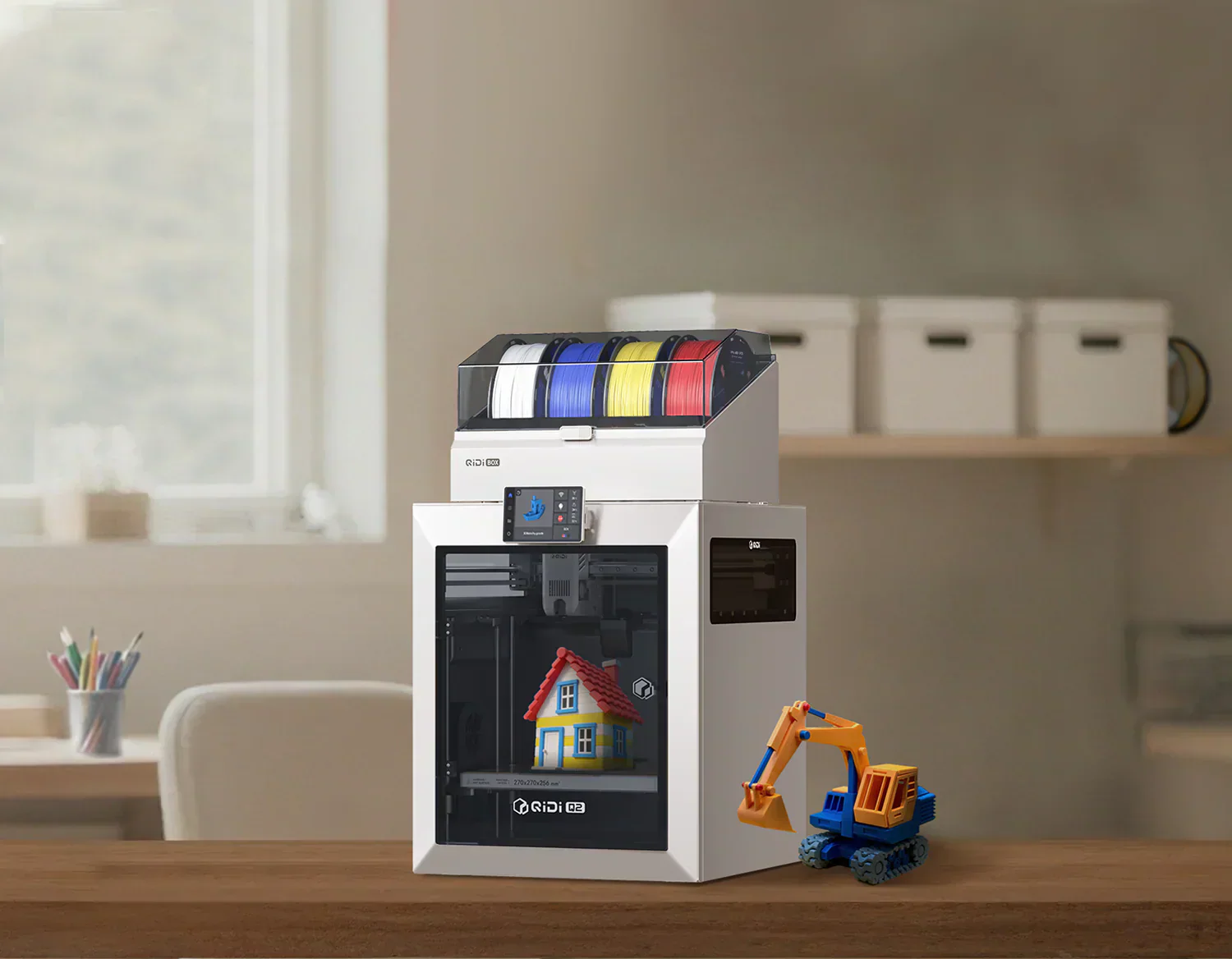 おもちゃの掘削機の横に、マルチカラーのフィラメントスプールを備えた QIDI 3D プリンターで家の模型を印刷しています。